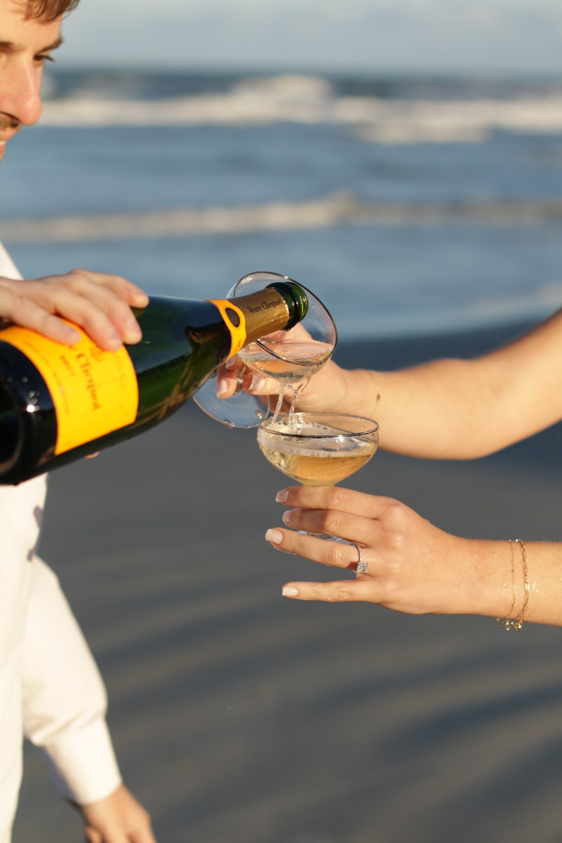 Newly engaged couple pouring champagne on the beach at sunset