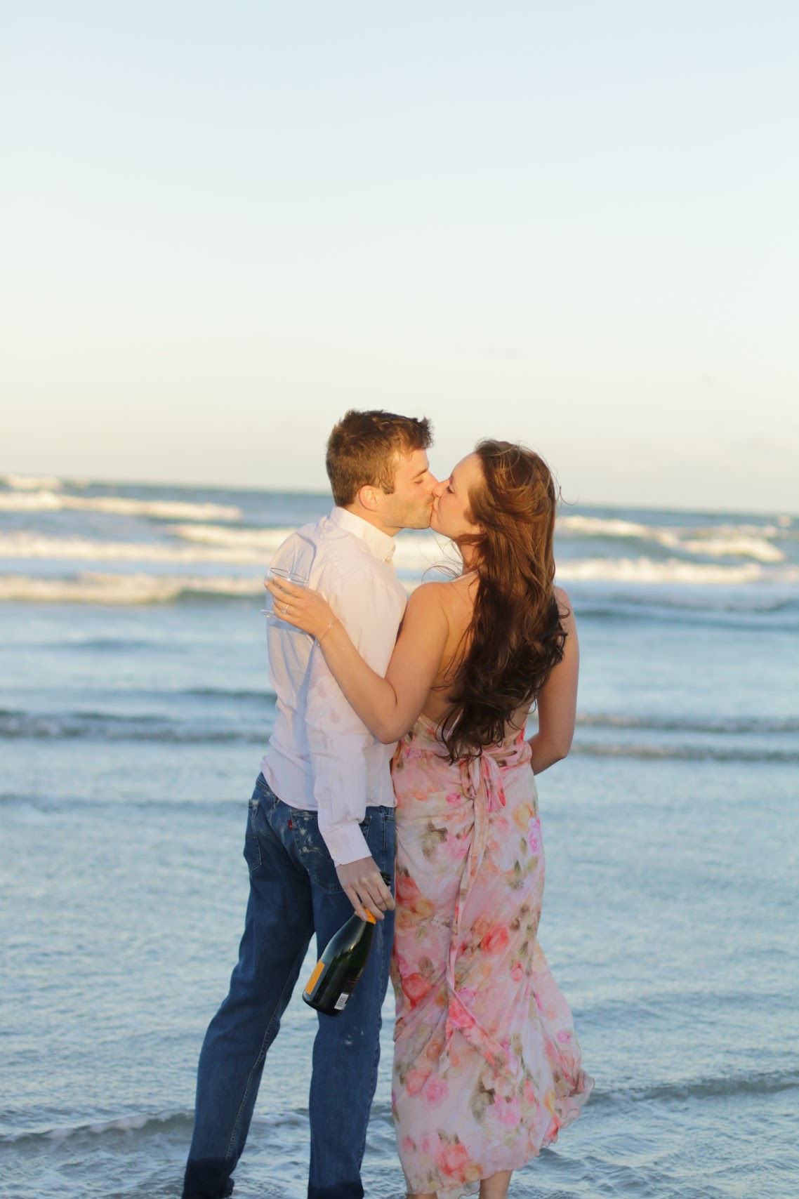 Engaged couple kissing in the surf with champagne